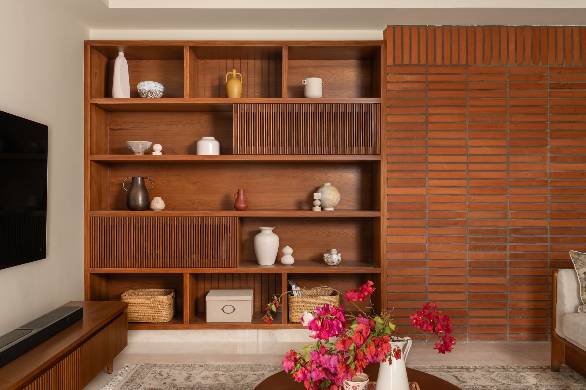 The living room's display wall, where fluted timber sliding panels and open shelving compose a surface meant to be read, not simply stored against