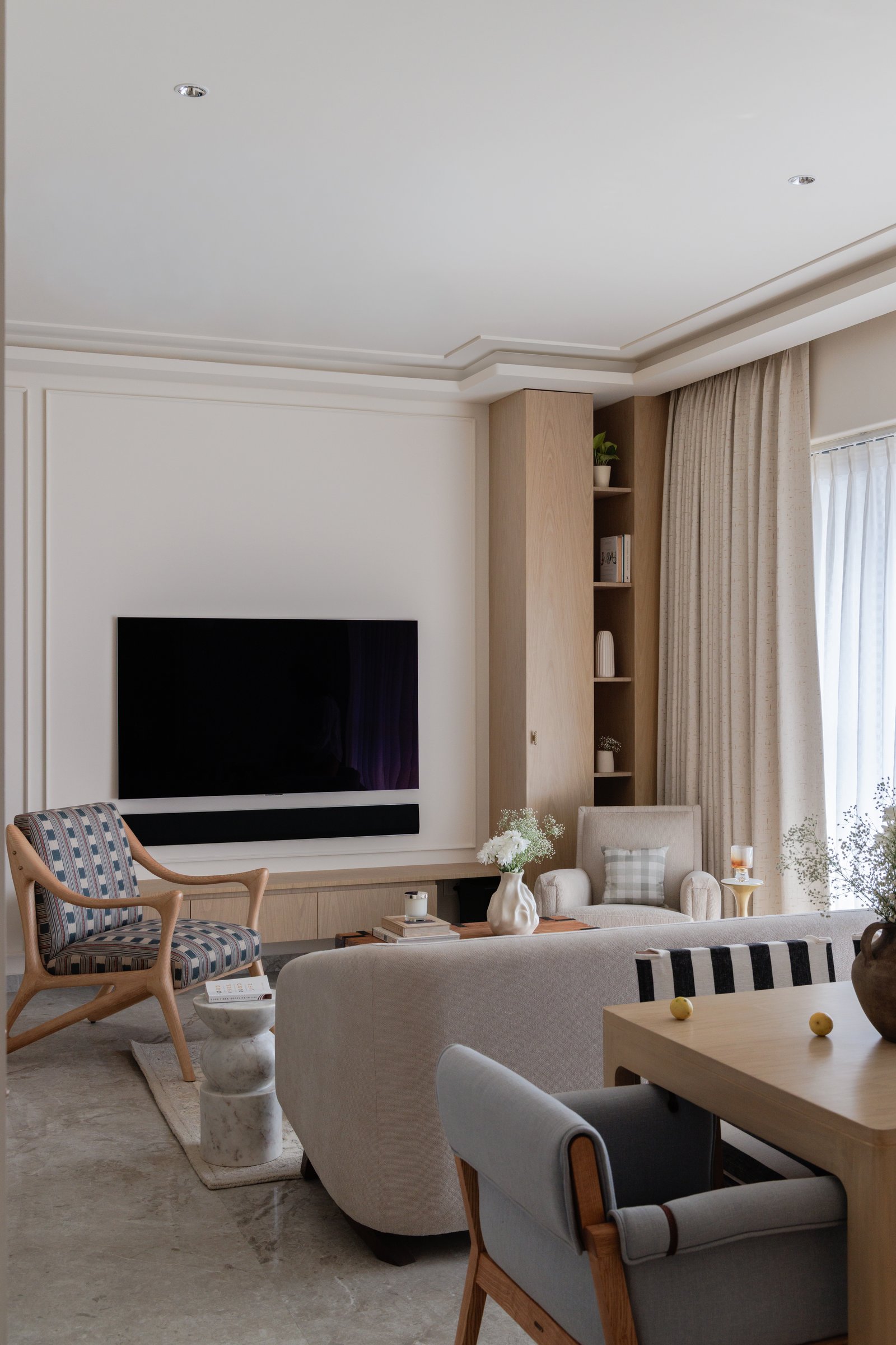 The living room's television wall, with stepped ceiling detail and a timber shelving unit that absorbs storage into architecture