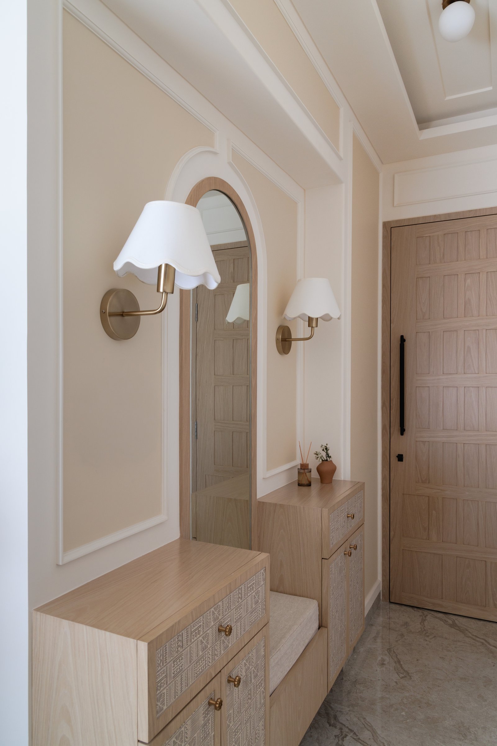 The entry foyer, where an arched mirror and scalloped brass sconces establish the home's tonal warmth from the first step