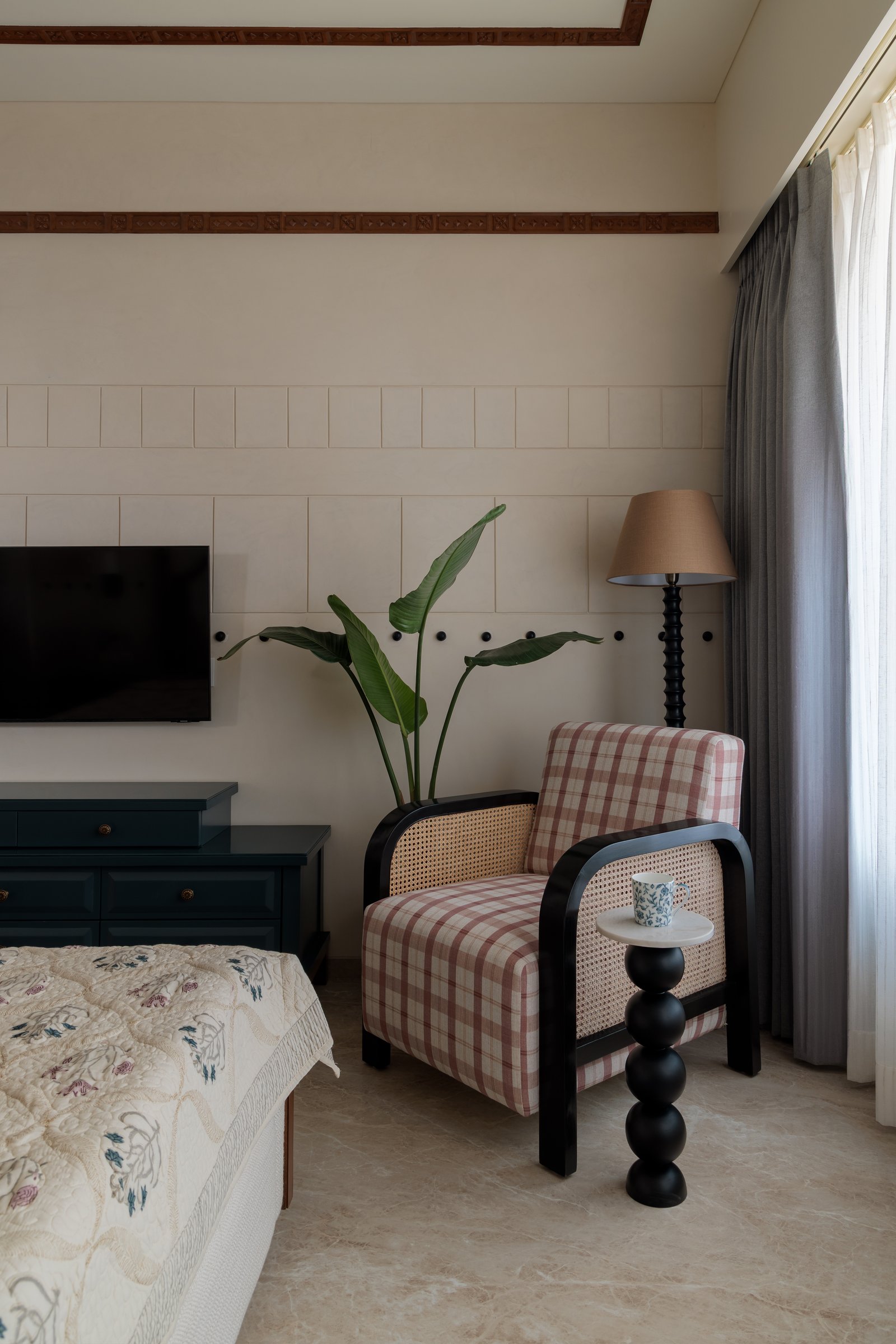 A gingham armchair with cane-woven panels and a sculptural side table anchor the master bedroom's reading corner