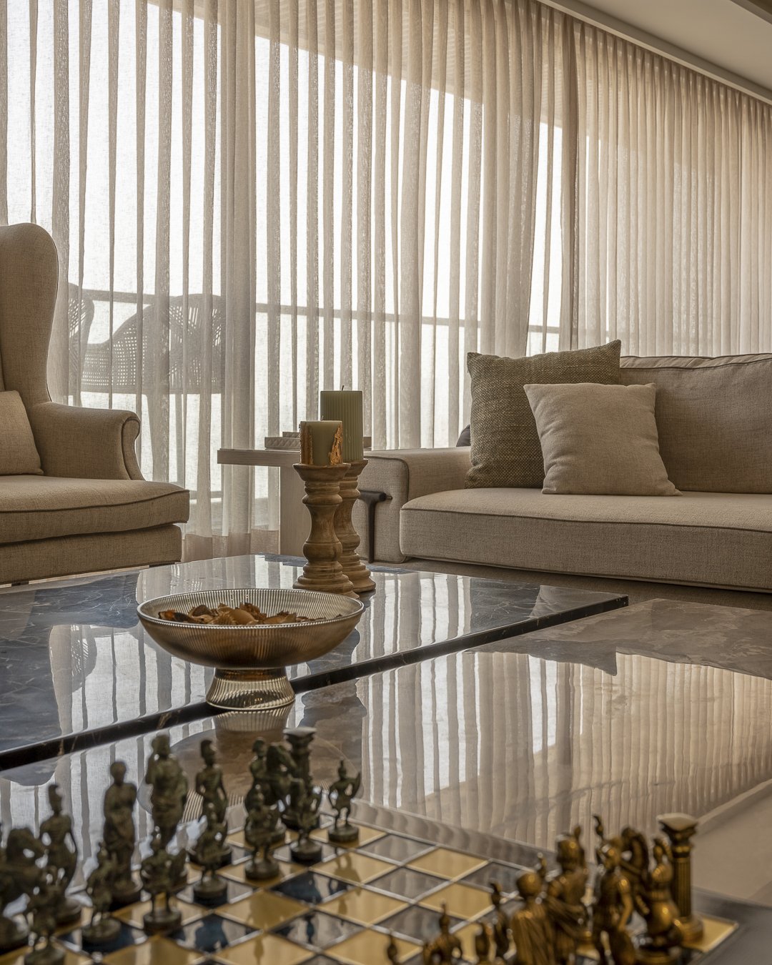 Sheer curtains diffuse coastal light across the living room's low, tightly composed seating arrangement